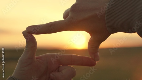 Girl shows her fingers frame symbol, sun. Hands of young female director cameraman making frame gesture at sunset in park. Sees like in movies. Concept of seeing world as different. Business planning