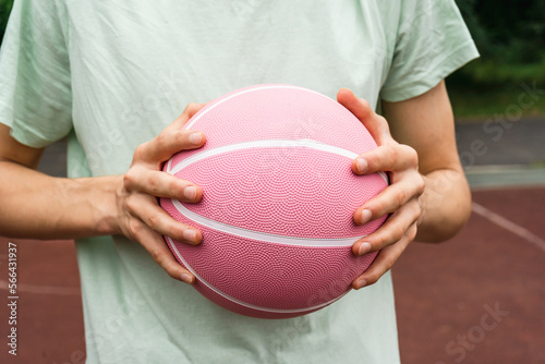 Pink basketball ball in man's hands in front of a basket outdoors. Minimal sport background. Sports gear, close up  © Natali