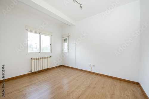 Empty living room with white walls  laminate flooring  white aluminum windows on two walls with blinds and a radiator below