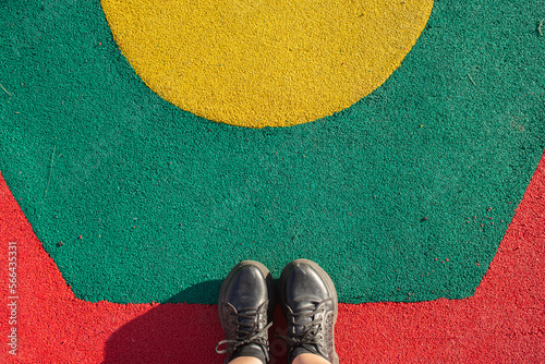 Mis pies con zapatillas sobre piso colorido en plaza de juegos 