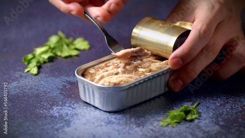Hand with a fork picking up canned mackerel on a dark blue table with parsley. Ready to eat.