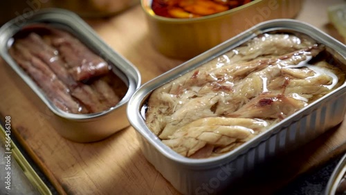 Preserve cans with different products, fish and seafood, natural or pickled, open on a dark table with a wooden cutting board and lemon. Ready to eat.