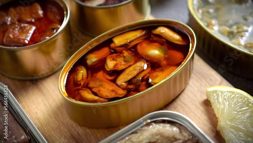 Preserve cans with different products, fish and seafood, natural or pickled, open on a dark table with a wooden cutting board and lemon. Ready to eat.