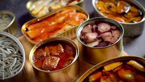 Preserve cans with different products, fish and seafood, natural or pickled, open on a dark table with a wooden cutting board and lemon. Ready to eat.