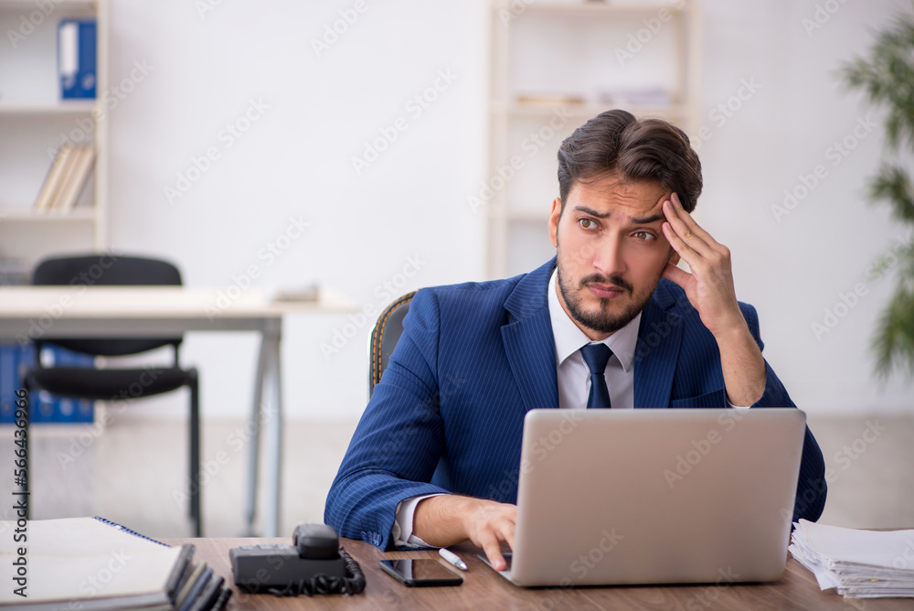 Young male employee unhappy with excessive work in the office Young male employee unhappy with excessive work in the office
