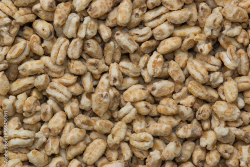 Dry honey puffed wheat cereal pieces scattered loosely directly above. Breakfast foods textured background, full frame image.