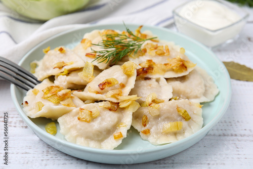 Cooked dumplings (varenyky) with tasty filling, fried onions and dill on wooden table, closeup