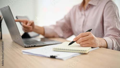 A businesswoman working at her desk, using laptop and taking notes on her notepad.