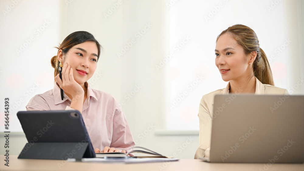 Two Asian businesswomen working on a marketing plan together, discussing planning their project Two Asian businesswomen working on a marketing plan together, discussing planning their project