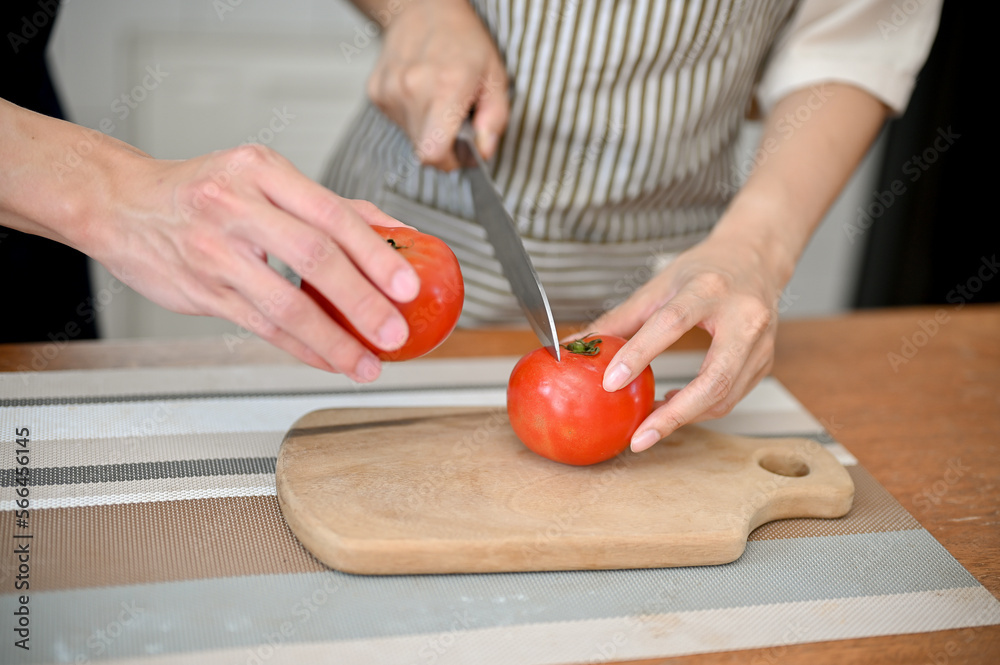 Close-up of couple preparing salad's ingredients together, cutting tomatoes on chopping board. Close-up of couple preparing salad's ingredients together, cutting tomatoes on chopping board.
