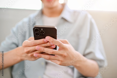 close-up image of a young Asian man relaxing on sofa in his living room, using his phone