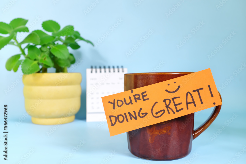 You're doing great words of encouragement concept. Selective focus of a cup of coffee with handwritten bright paper message note.