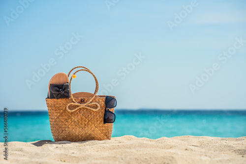 A bag on a tropical beach. Sunglasses and flip-flops in a woven bag on white sand against the background of the sea or ocean