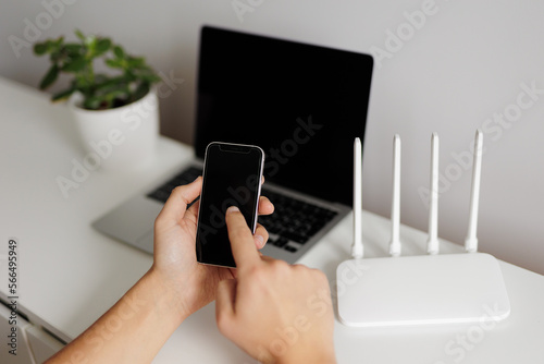 wifi connection concept - hand with phone in the foreground and computer with router on background