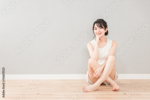 家のリビングに座って頬杖をつく美人のアジア人女性（美容・ダイエット・エステ・脱毛・コピースペース）