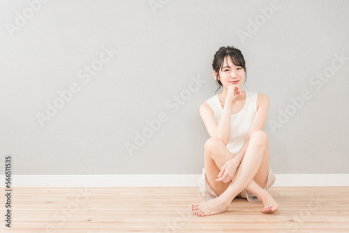 家のリビングに座って頬杖をつく美人のアジア人女性（美容・ダイエット・エステ・脱毛・コピースペース）