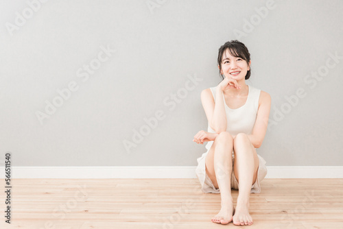 家のリビングに座って頬杖をついて考える美人のアジア人女性（美容・ダイエット・エステ・脱毛・美脚）