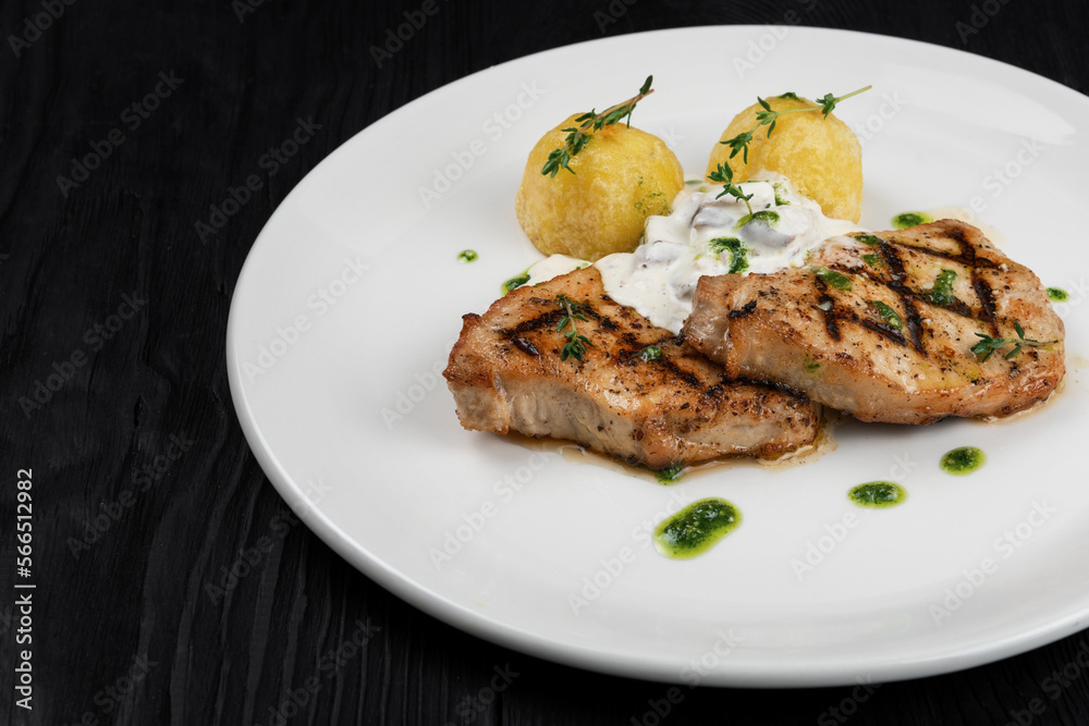 Grilled pork meat with mushroom sauce and potato on white plate on wooden black background Grilled pork meat with mushroom sauce and potato on white plate on wooden black background