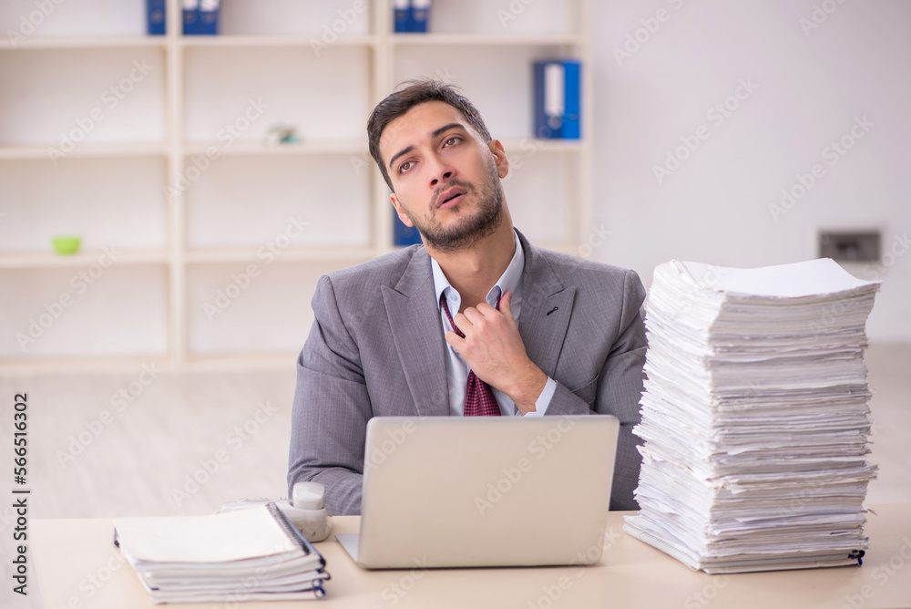 Young male employee unhappy with excessive work in the office Young male employee unhappy with excessive work in the office
