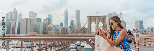 New York woman using phone app walking on Brooklyn Bridge by Manhattan city skyline. Young female professional multicultural lady, New York City, USA. Panoramic banner
