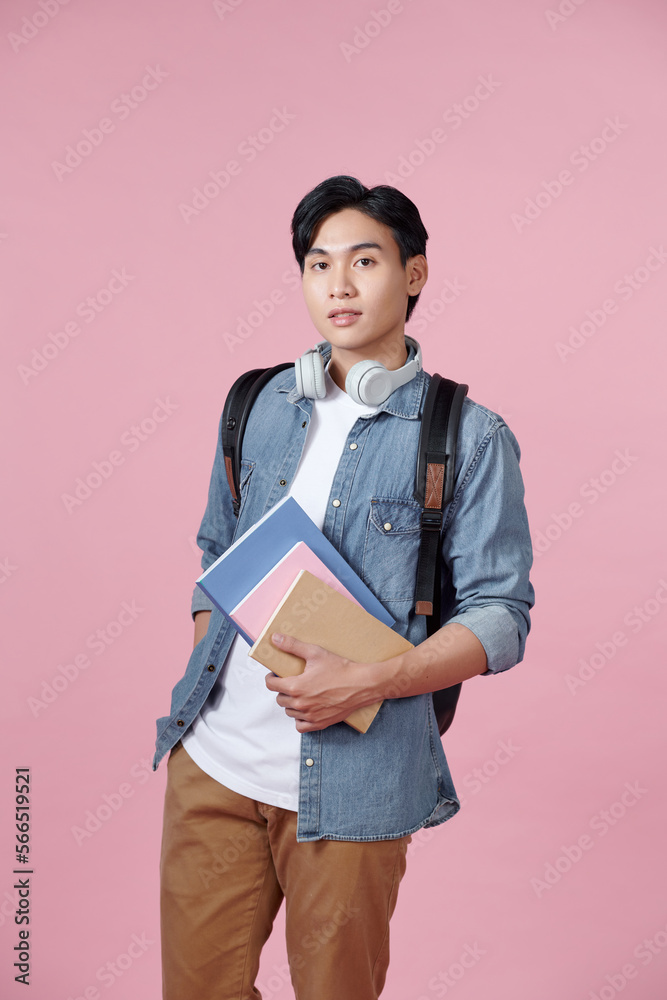 Portrait of smiling young college student with books and backpack against pink background Portrait of smiling young college student with books and backpack against pink background