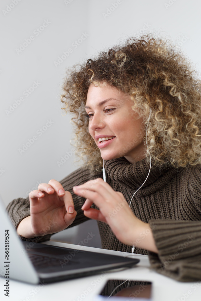 Fototapeta premium Portrait of cute curly female person in headset talking on video call. Young woman speaks on web camera during internet conference