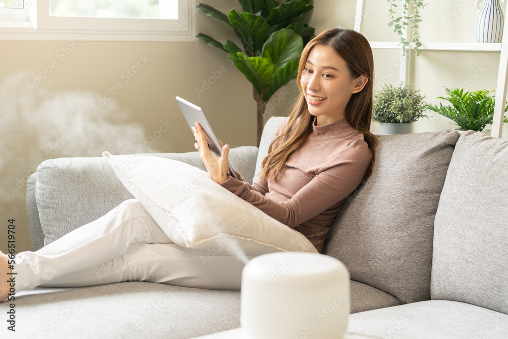 Air humidifier, happy asian young woman, girl using tablet on sofa, enjoy aromatherapy steam scent from essential oil diffuser comfortable while rest in living conditions room, apartment at home. Air humidifier, happy asian young woman, girl using tablet on sofa, enjoy aromatherapy steam scent from essential oil diffuser comfortable while rest in living conditions room, apartment at home.