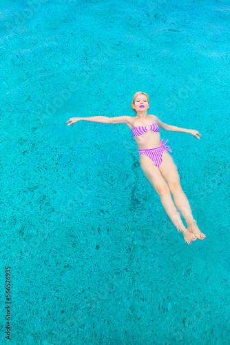 Glamorous woman in a swimming costume swims in a pool in blue water. View from above