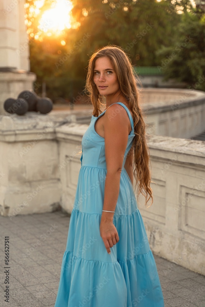 Woman sunset blue dress. Portrait of a woman with long hair and a blue dress against the backdrop of the setting sun and a white building. Lifestyle, walking around the city