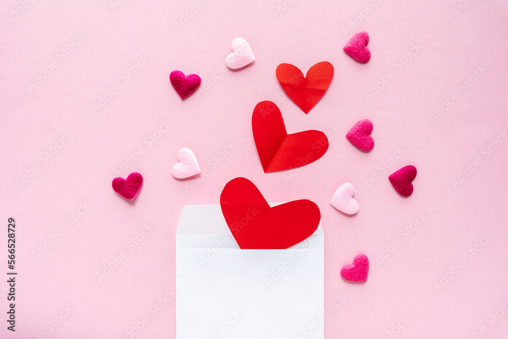 Ein weißes Briefkuvert gefüllt mit verschiedenen Herzen auf einem rosa Hintergrund. Flat lay, Valentinstag.