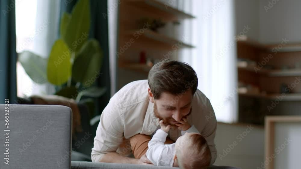Young happy dad playing with his newborn baby daughter, blowing at her, carefree girl laughing, empty space Young happy dad playing with his newborn baby daughter, blowing at her, carefree girl laughing, empty space