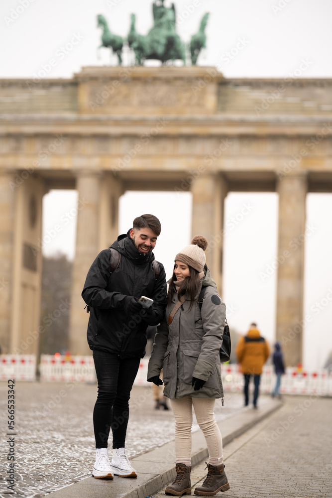 Friends smiling while searching for information on smartphone with Brandenburg Gate in the background in Berlin, Germany - tourism concept.