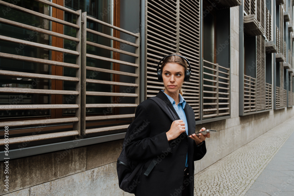Young woman using headphones and mobile phone while walking at city street Young woman using headphones and mobile phone while walking at city street