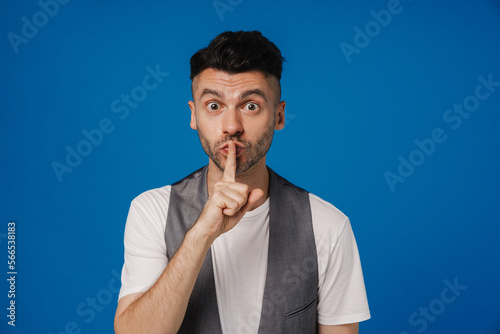 Young white man holding finger at mouth while gesturing silence sign