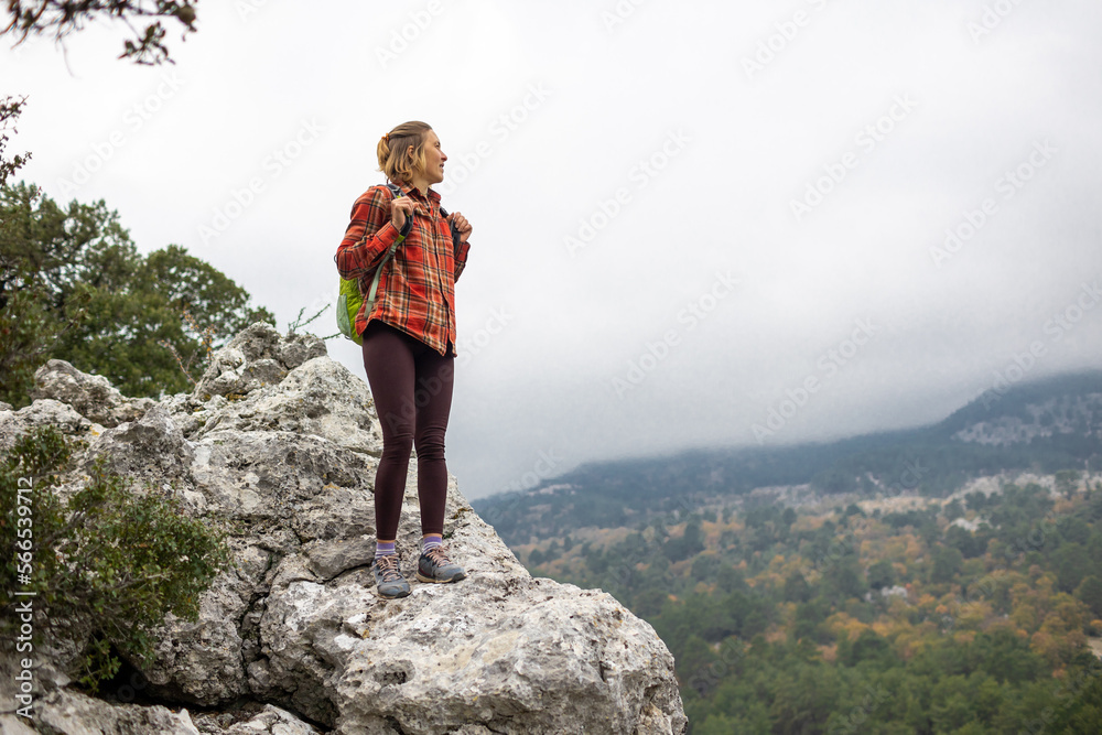traveler girl stands on the edge of a cliff with an autumn forest and enjoys a beautiful view of the valley.