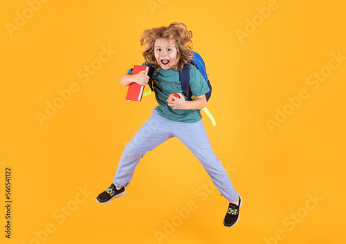 Funny child school boy jumping on a yellow studio background.