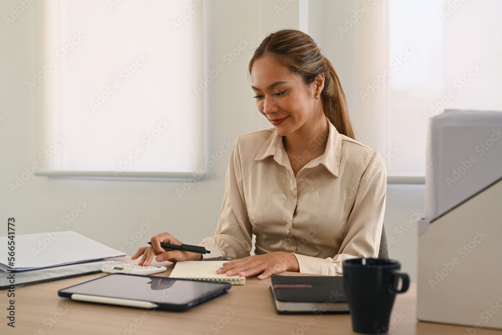 Smiling female employee using calculator, preparing financial reports at her office desk Smiling female employee using calculator, preparing financial reports at her office desk