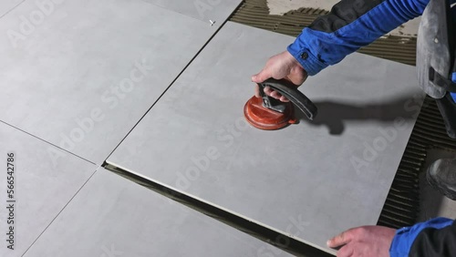 Tiler worker placing or tiling gray ceramic tile in the position over adhesive glue with lash tile leveling system, renovation or recontruction, concept of building