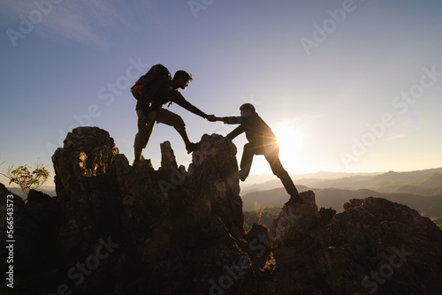  Silhouettes of two people climbing on mountain and helping. Help and assistance concept. © Tinnakorn