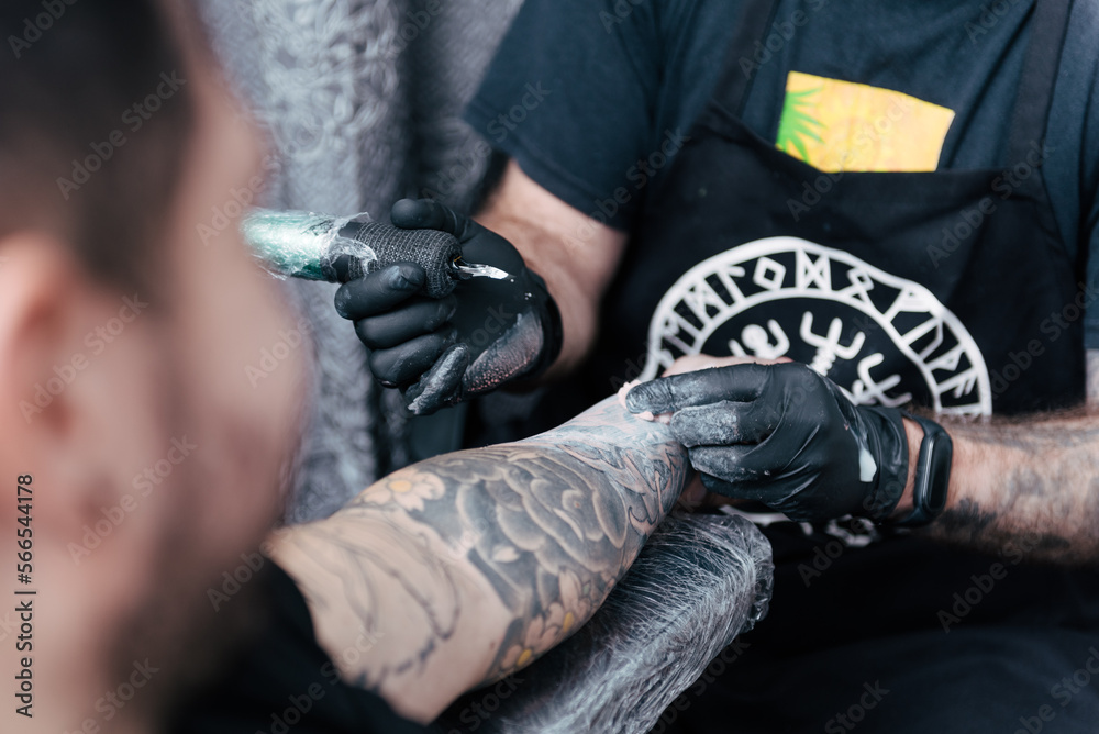 Client point of view being tattooed. Working on process on arm with white ink. Detailed hands with black gloves tattooing. Creative small business and tattoo master. 