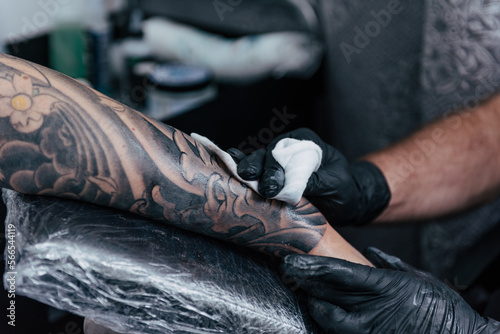 Close up tattooist cleaning fresh tattoo. Final process on forearm with white ink. Detail black gloves tattooing. Tattoo artist working in studio. Creative small business and tattoo master.