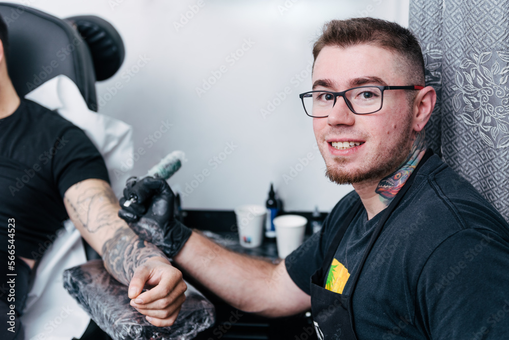 Fototapeta premium Young tattoo artist portrait smiling and looking at camera tattooing on studio. Tattooist. White background.