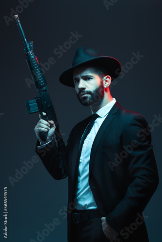 Man, suit or automatic rifle on dark studio background in secret spy, isolated mafia or crime lord security. Model, gangster or thinking hitman and gun in stylish, trendy or fashion clothes aesthetic