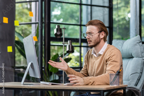 Frustrated and upset businessman reading news online from computer monitor, young blond man sad at workplace inside office in casual clothes unhappy with results.