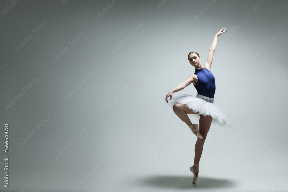 Fototapeta premium Young ballerina practicing dance moves on grey background. Space for text