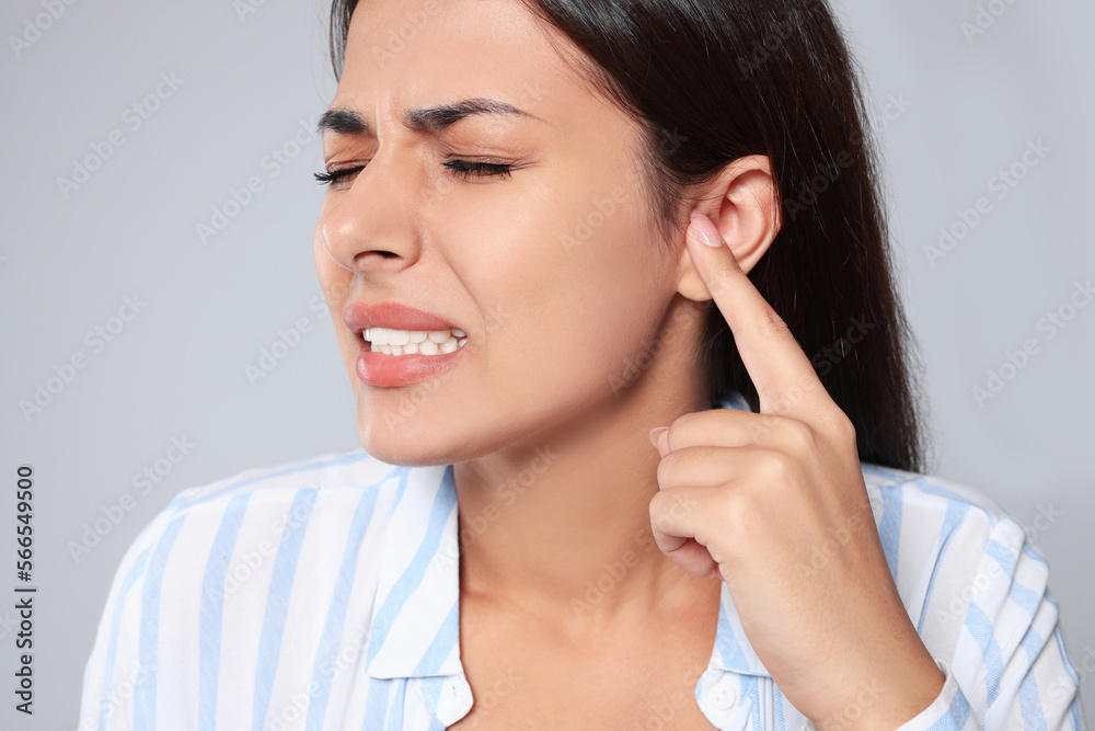 Emotional young woman suffering from ear pain on light grey background, closeup Emotional young woman suffering from ear pain on light grey background, closeup