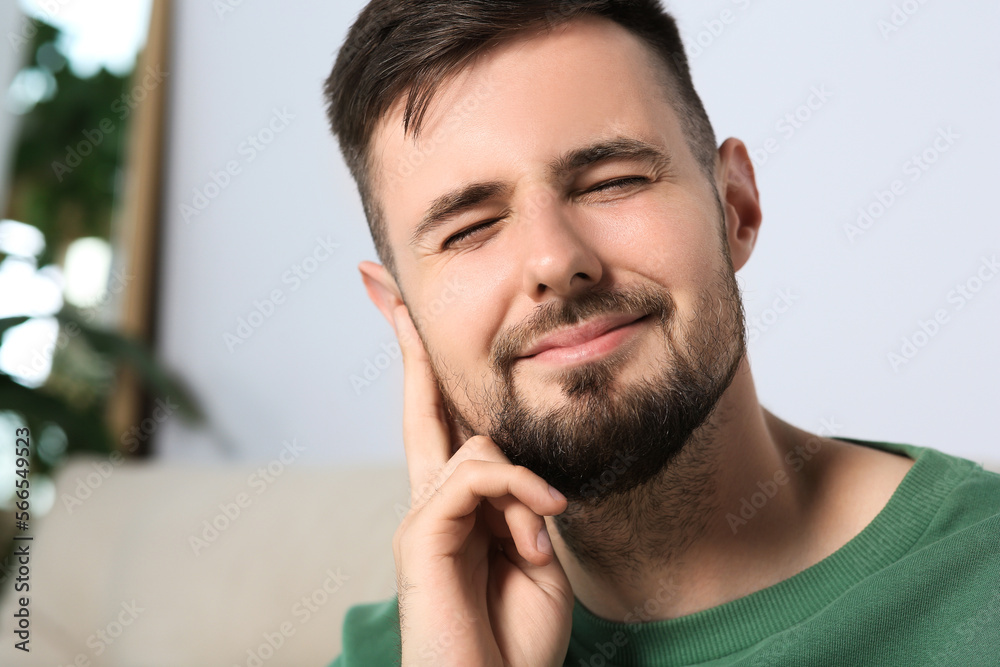 Young man suffering from ear pain at home. Space for text