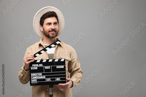 Smiling actor holding clapperboard on grey background, space for text