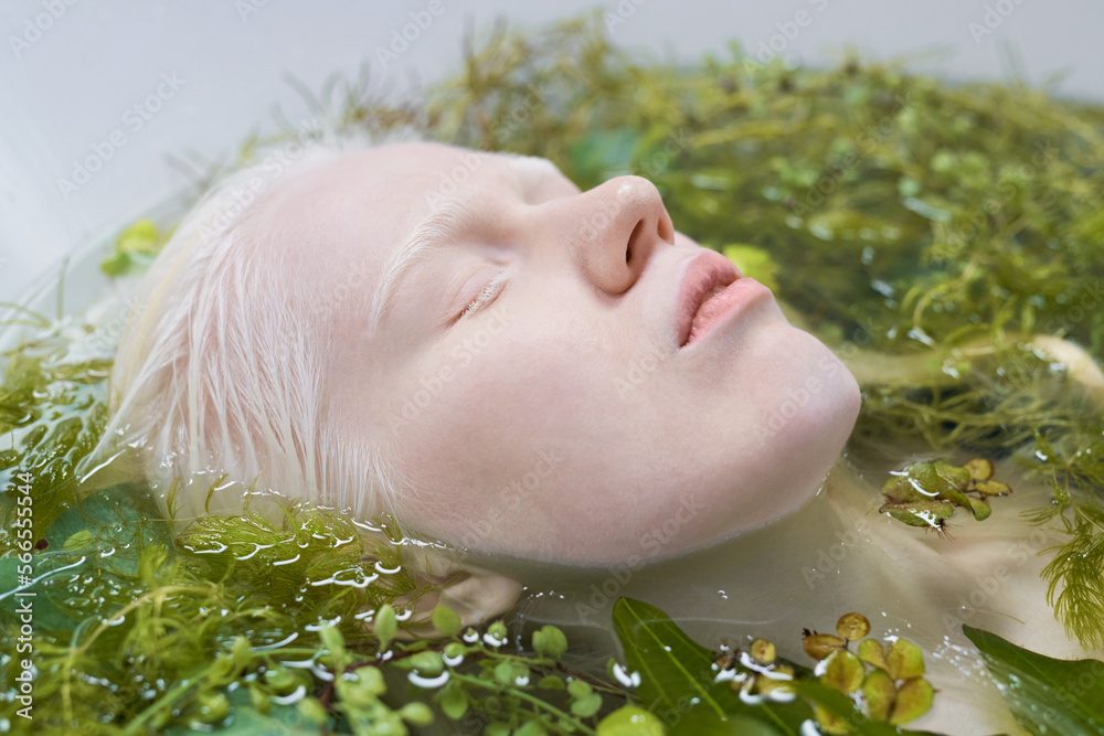 Φωτογραφία Close-up of pale face of albino girl lying in bath with warm pure water and gree