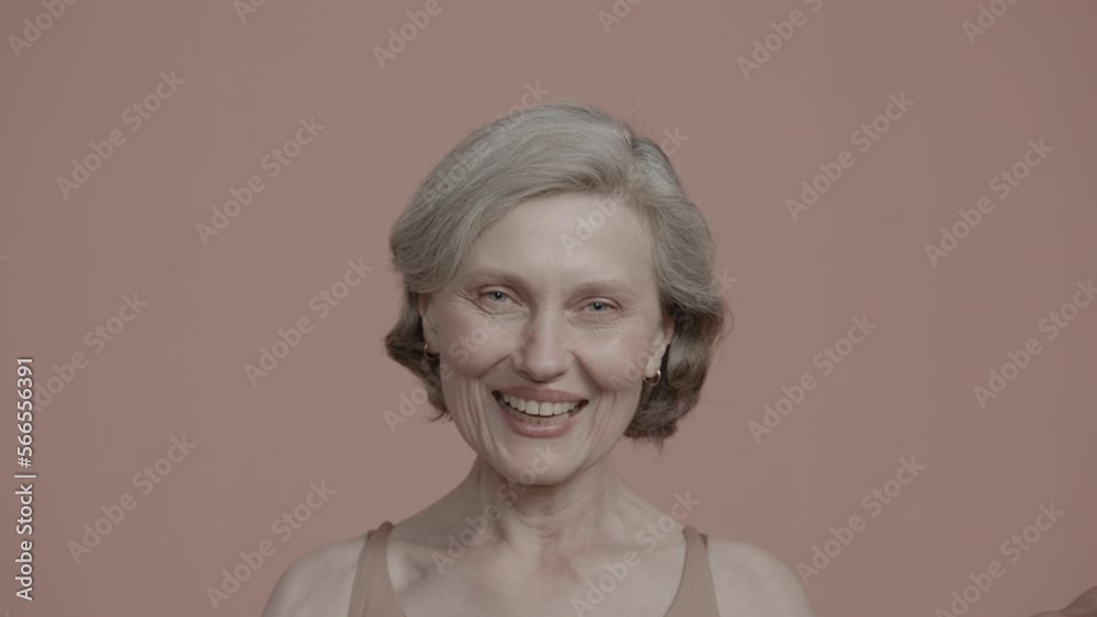 Portrait of 60s adult mature Caucasian female smiling and laughing at camera against pastel colored background Portrait of 60s adult mature Caucasian female smiling and laughing at camera against pastel colored background